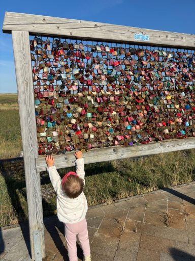 Kleines Kind versucht, ein buntes Liebesschloss-Gitter zu erreichen.