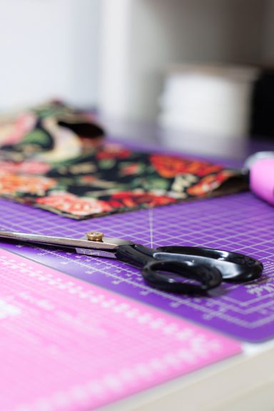 Schneiderwerkzeuge auf einem Tisch mit buntem Stoff und einer Schneidematte.