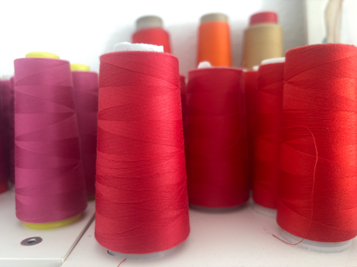 Bunte Garnspulen in verschiedenen Rottönen stehen nebeneinander.