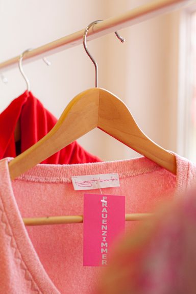 Rosa Kleidung auf einem Holzkleiderbügel mit Preisschild in einem hellen Raum.