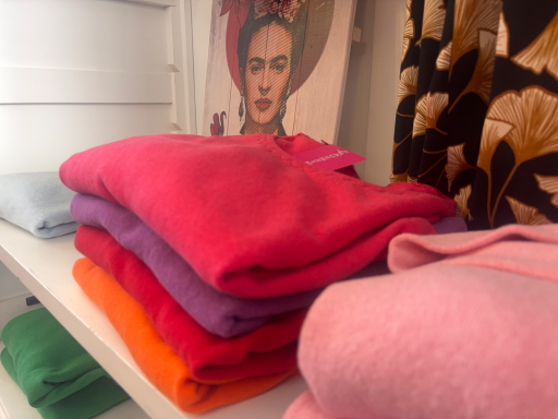 Bunte Stoffstapel in verschiedenen Farben auf einem Regal, im Hintergrund ein Kunstwerk.