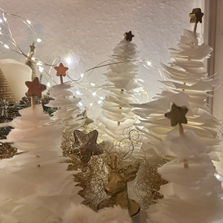 Weiße Weihnachtsbäume mit goldenen Sternen und funkelnden Lichtern im Hintergrund.