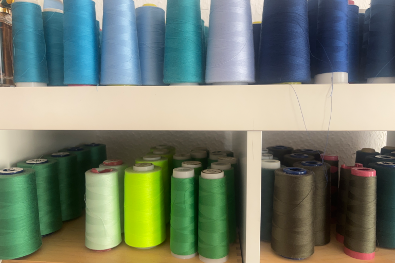 Farbige Nähgarne auf Regal, in verschiedenen Grüntönen und Blau, mehrere Spulen sichtbar.