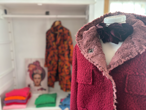 Rote Jacke im Vordergrund, bunte Kleidung und ein Frida Kahlo-Porträt im Hintergrund.