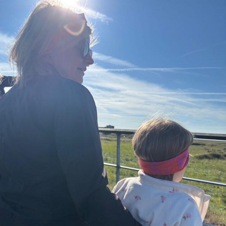 Frau mit Sonnenbrille hält ein Kind, beide schauen in die Ferne bei sonnigem Wetter.