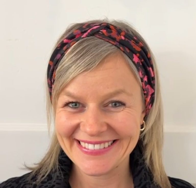 Lächelnde Frau mit blonden Haaren und buntem Stirnband.